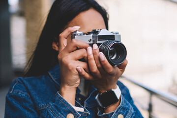 Young dark skinned hipster girl in jeans jacket spending time on hobby taking pictures on city...