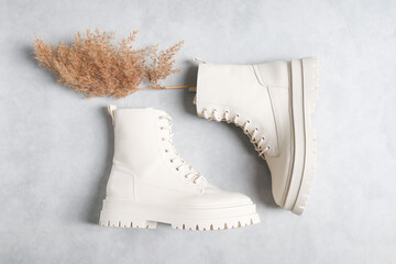 White demi-season boots and a dry cane branch on a gray cement background. .