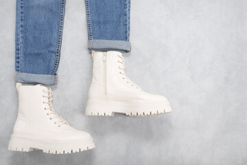 White demi-season boots and blue jeans on a gray cement background.