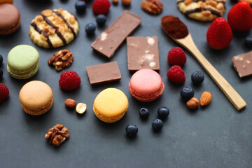 Macarons, chocolate, cookies, berries and various nuts on dark blue background. Selective focus.