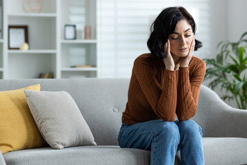 Woman sitting on couch feeling stressed and sad at home