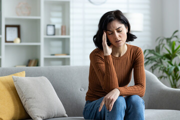 Woman sitting on couch feeling stressed, suffering from headache or migraine at home, dealing with...