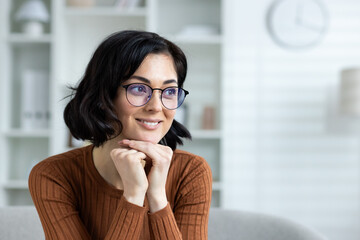 Smiling woman with glasses sitting indoors in a cozy home environment