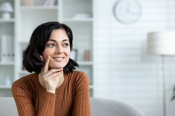 Smiling woman in casual attire thinking while sitting in modern living room
