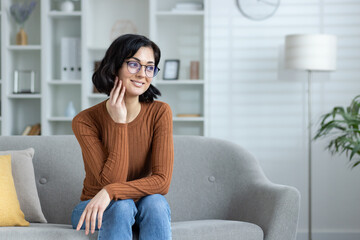 Smiling woman with glasses sitting on couch in cozy living room