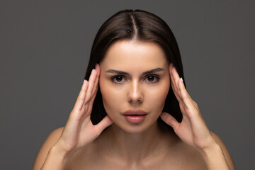 Portrait of woman with natural nude make up with bare shoulders on gray background.