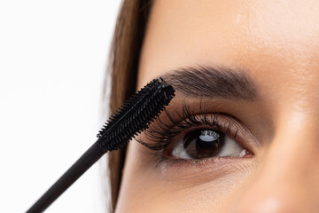 Young woman putting eye liner on eyelid on white background