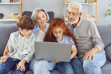 Happy family with grandchildren relaxes on the couch at home, enjoying online entertainment on a...