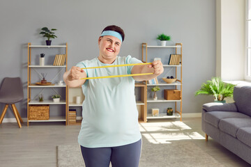 Portrait of a fat funny smiling happy woman doing sport stretching exercises with rubber band in...