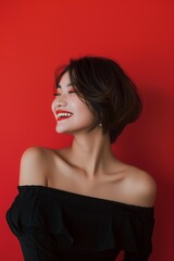 Fototapeta premium Portrait of a stylish Asian woman with short hair and bold makeup, illuminated by dramatic lighting against a vibrant red background.