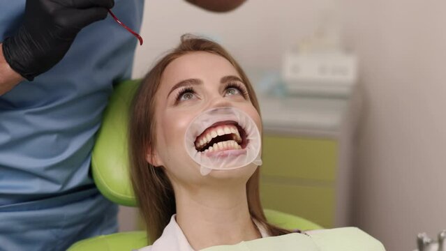 Protective eyewear, Dental mask, Dental patient. Dentist in blue scrubs and mask adjusting protective eyewear on smiling patient with mouth retractor in dental chair.