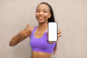 Happy Latin lady holding smartphone with blank screen and showing thumb up, recommending new workout application, mockup, selective focus