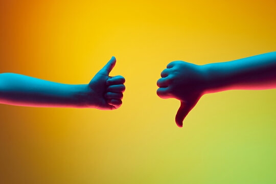Opposing Opinions. One hand offers thumbs up in approval, while other hand delivers thumbs down in disapproval. Copy space for ad. Gradient background in neon light
