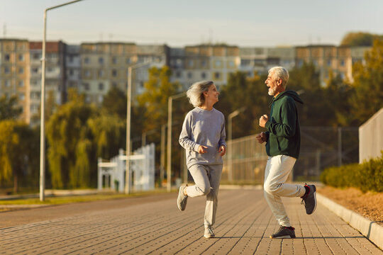 Happy old married couple learn physical vitality and longevity secret, do sport workout, have fun. Cheerful joyful older male female friends work out, run together in park on good spring or summer day