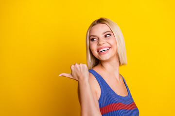 Photo portrait of young beautiful woman promoter looking and pointing finger empty space repost video isolated on yellow color background