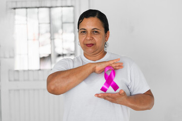 brunette latin adult woman, showing the pink ribbon that she wears on her chest as a symbol of the...
