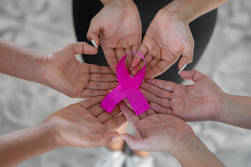 group of women joining hands to hold a pink ribbon, symbol of the fight against breast cancer.
