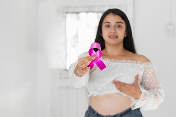 caucasian latina woman, showing a pink ribbon, symbol of breast cancer, while touching her breast...