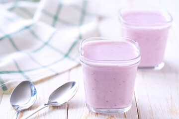Two portions of homemade fruit yogurt in a glass jars on a white table, selective focus.
