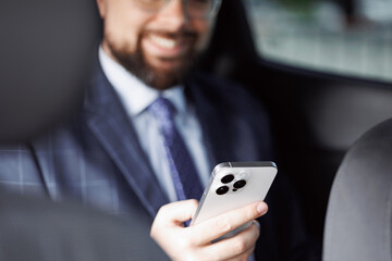 Close-up businessman using modern white smartphone while sitting car. Reads news or uses app or online internet. Modern technologies. Car steering wheel. Male hand holding smartphone