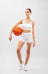 A beautiful slender girl athlete in white shorts and in top plays basketball.