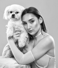 A young beautiful girl in a pink dress with a white small dog on a pink background.
