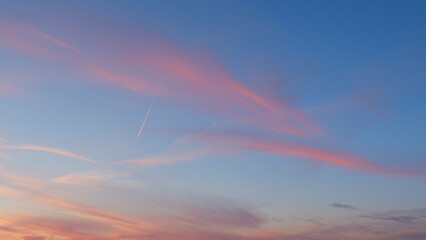 Beautiful jet contrail as airplane streaks across sky. Pink orange red blue clear sunset or sunrise sky, white and pink soft gradient clouds. Timelapse. - Powered by Adobe