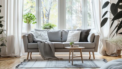 A serene and stylish living room featuring a comfortable gray sofa, surrounded by indoor plants and bathed in natural light from large windows.