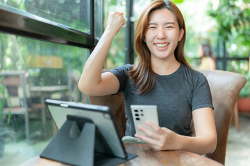 Asian woman sitting at work in a coffee shop holding a cell phone and smiling happily after...