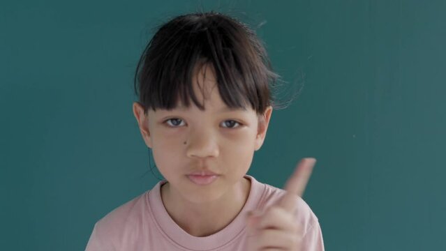 Portrait of a cute Asian Thai kid girl, 8 to 10 years old, raising her hand to kiss her lips. It is a scolding for not making a loud noise or stopping an action. Background is green screen