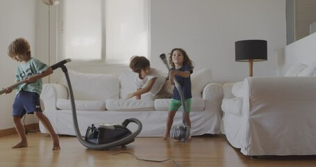 Three kids are joyfully cleaning a living room with a vacuum, appearing to dance and enjoy their housework.