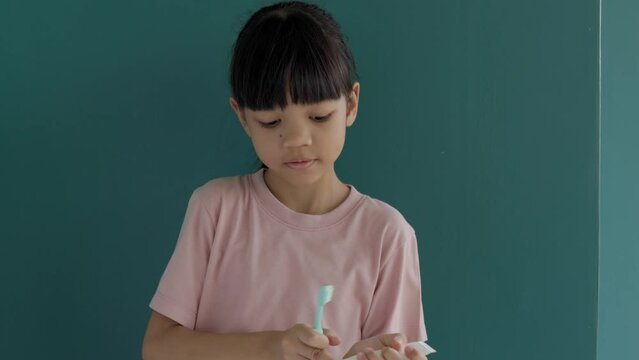 Portrait Thai Asian kid girl, aged 8 to 10 years, has a cute and bright face. He is making a gesture of squeezing toothpaste onto a toothbrush. and pretend to brush your teeth, background is green.