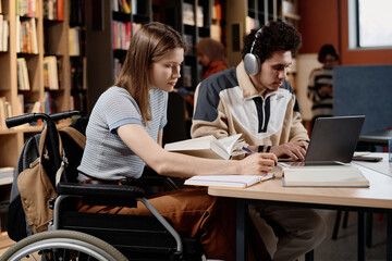 Young female student with disability and her male friend doing homework together at university library