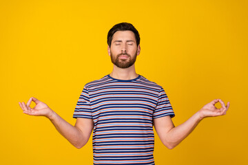 Photo of calm positive pleasant man with stylish beard dressed striped t-shirt meditating close...