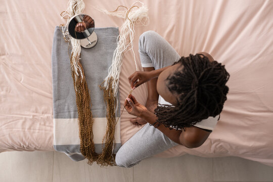 Woman braiding hair with threads near mirror on bed