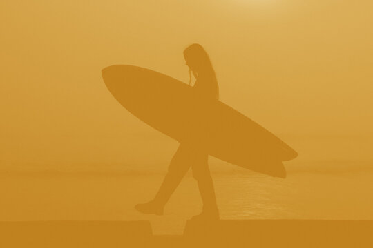 silhouette of woman with surfboard with yellow hue