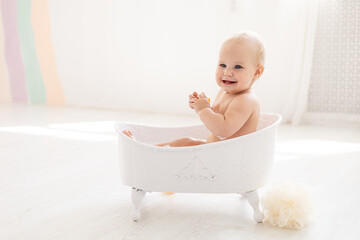 a little baby girl of six months with blue eyes bathes in a bubble bath and plays with rubber toys...