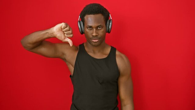 Pissed-off young african american man, thumbing down the music he's hearing, expressing rejection over a stark red background
