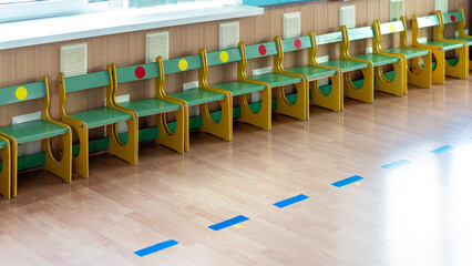 Row of green and yellow school desks with chairs, colorful dots on backrests. Empty classroom...