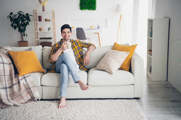 Photo of funny positive man wear checkered shirt staying home enjoying coffee sitting couch indoors...
