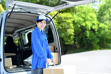 外で台車で荷物を運ぶ配送ドライバーの女性
