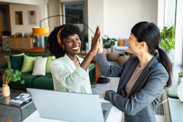 Two professional women celebrating success with a high-five in a stylish office