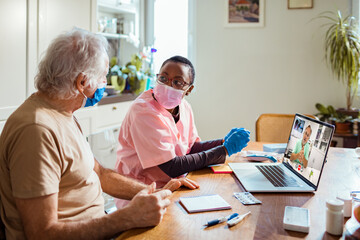 Nurse assisting elderly man with virtual doctor consultation at home