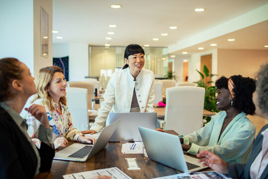Multiethnic female colleagues discussing work with laptops in a modern office