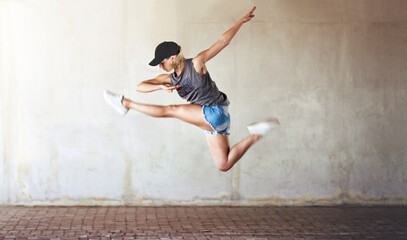 Woman, dancing and jump with city wall background or creative workout for hip hop, urban or...