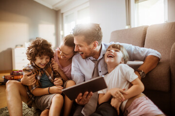 Parents and children using tablet on living room sofa