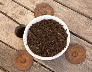 Gardening materials. Top closeup view of compost white bowl on the wooden table. Soil rich in...