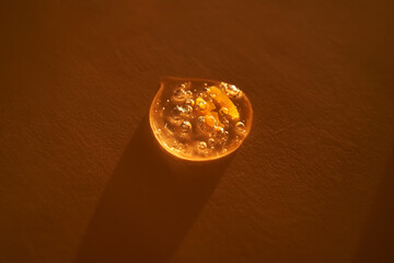 Drop of serum shimmering in the sun on a beige background.