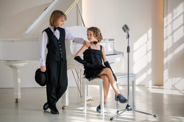 Two children dressed in black and white in front of a piano.