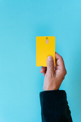 Close up of woman hand in blazer holding yellow debit card on turquoise background